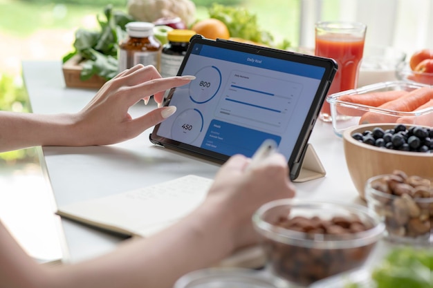 Woman professional nutritionist working and checking data from a laptop with a variety of fruits nuts vegetables and dietary supplements on the table