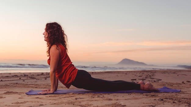 Woman in profile on beach performing back stretches