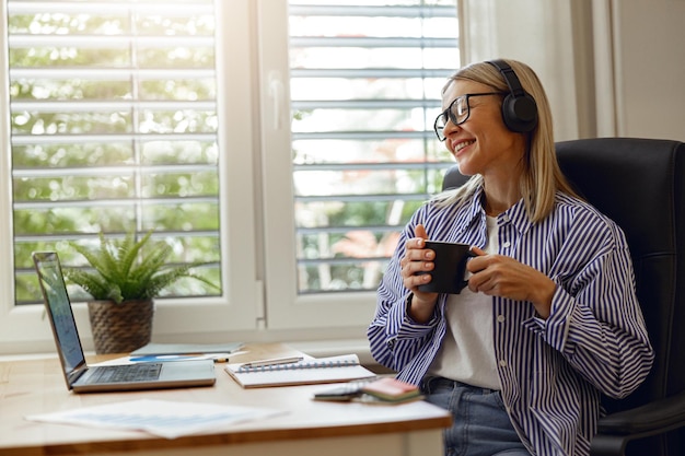 Woman programmer in headphones is enjoying coffee while working from home distance work concept