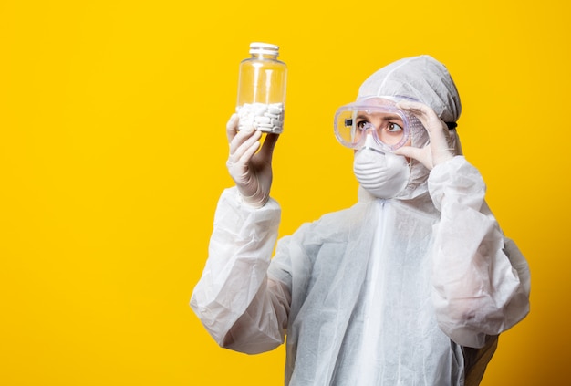 Woman in protection suit and mask holds jar with pills