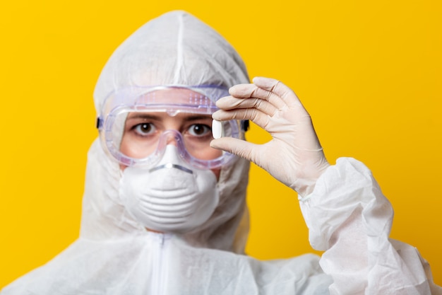 Woman in protection suit and mask holds pill