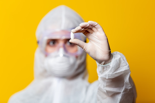 Woman in protection suit and mask holds pill