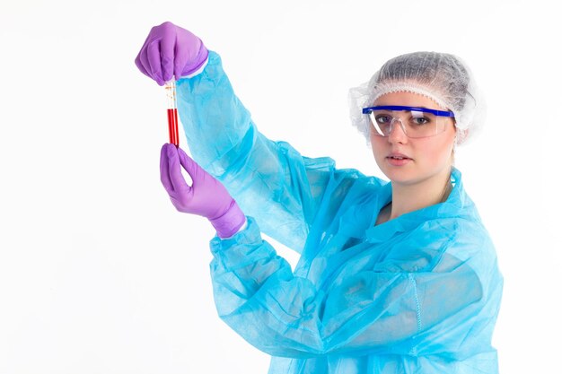 The woman in a protective coat with glasses is showing a tube with red liquid on a white background