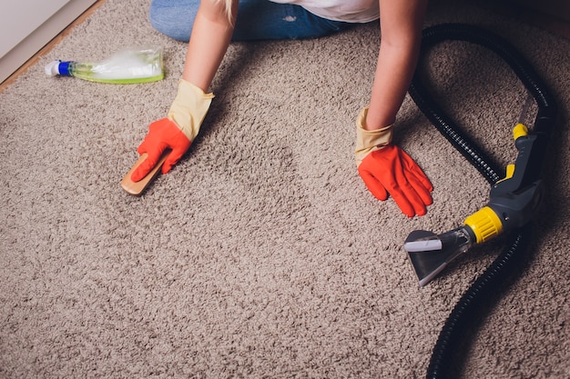 Photo woman in protective glove cleaning carpet with brush.