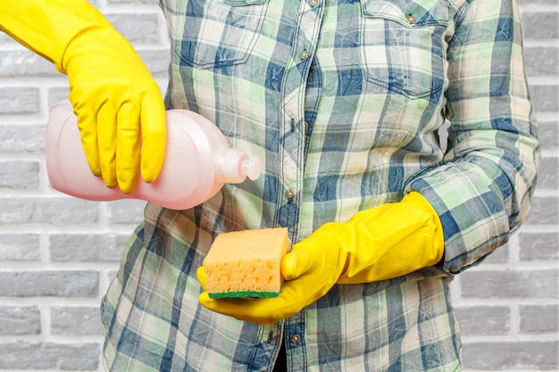 Женщина в защитной перчатке с бутылкой жидкости для мытья посуды