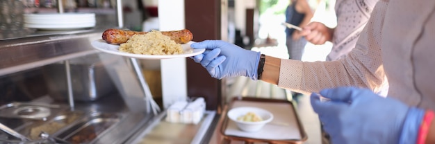 Woman in protective gloves in cafe takes plate of food.