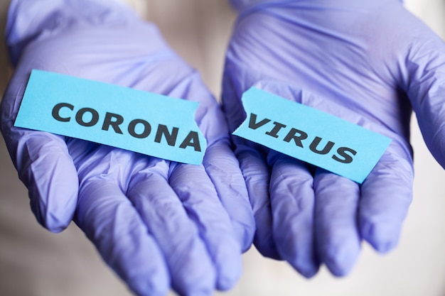 Woman in protective gloves holding inscription coronavirus