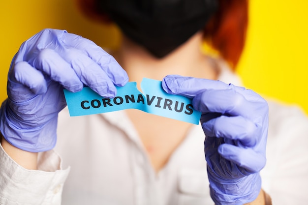 Woman in protective gloves holding inscription coronavirus