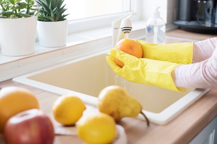 Woman in protective gloves washing fresh fruits at home on the kitchen, detergent in the foreground. Concept of hygiene during the coronavirus epidemic