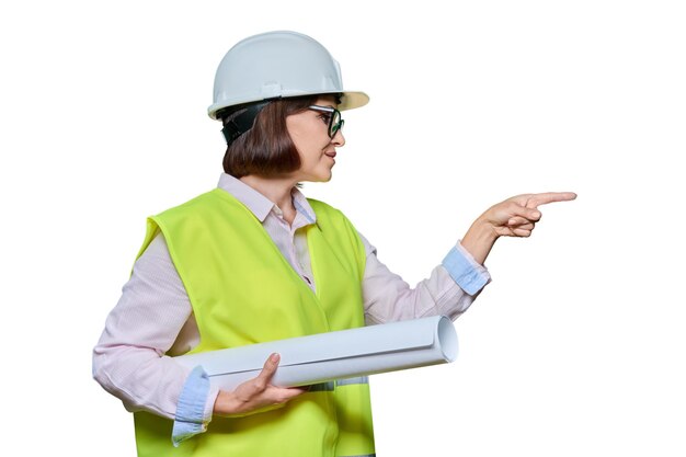 Woman in protective helmet points her finger at place for text Female industrial worker with blueprint standing in profile on white isolated background Construction engineering management building