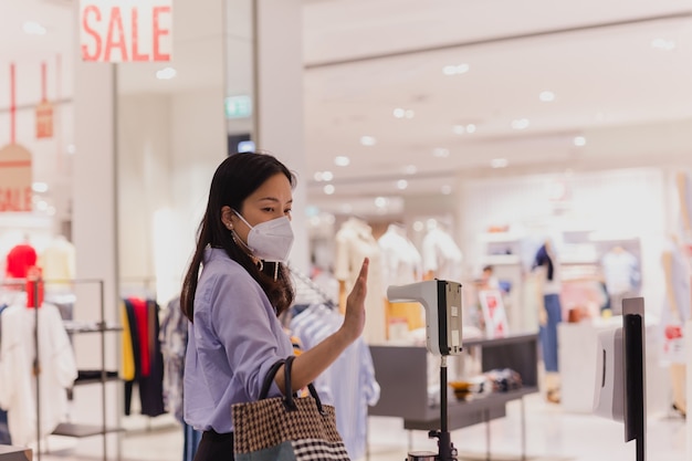 Woman in protective mask hand measuring thermometer temperature while entering shopping mall