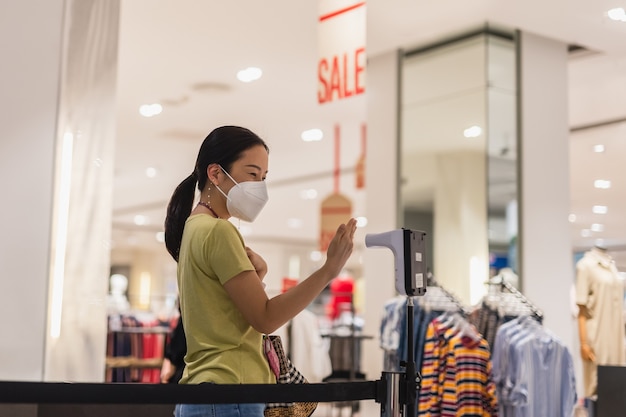 Woman in protective mask hand measuring thermometer temperature while entering shopping mall.
