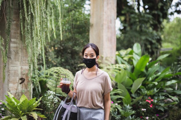 Woman in protective mask holding iced coffee