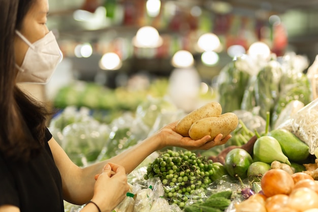 野菜店でジャガイモを保持している保護マスクの女性