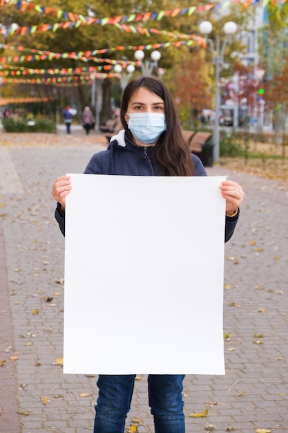 A woman in a protective mask holds a vertical sheet of paper without text