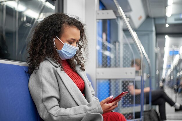 Woman in a protective mask talking on a video link sitting in a subway car