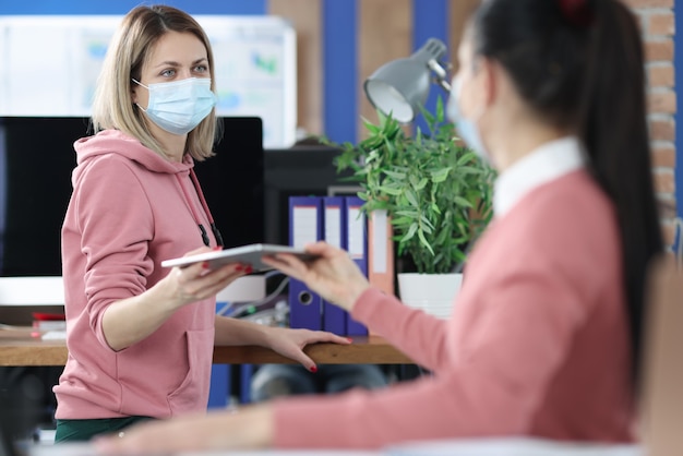 Женщина в защитной медицинской маске передает документы коллеге. Безопасность на рабочем месте в концепции пандемии коронавируса