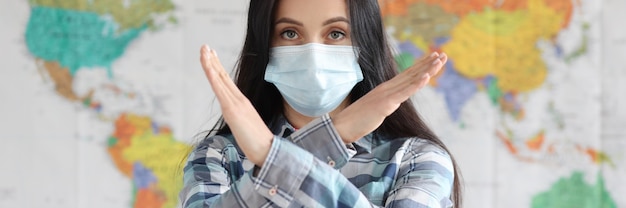 Woman in protective medical mask showing prohibiting gesture against background of world map