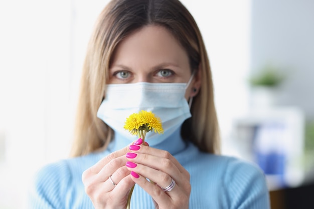 Donna in maschera medica protettiva che fiuta fiori gialli. perdita dell'olfatto come sintomo del concetto di covid19