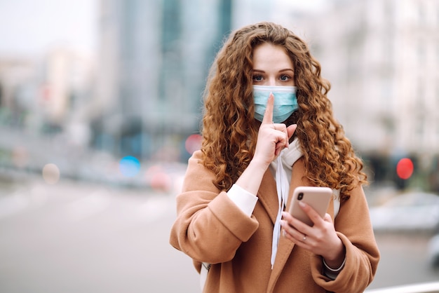 Woman in protective sterile medical mask on her face shows a gesture: shh. silence.