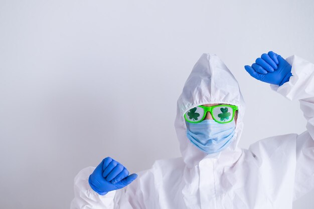 Foto una donna con una tuta protettiva e una maschera medica e indossando occhiali divertenti celebra san patrizio