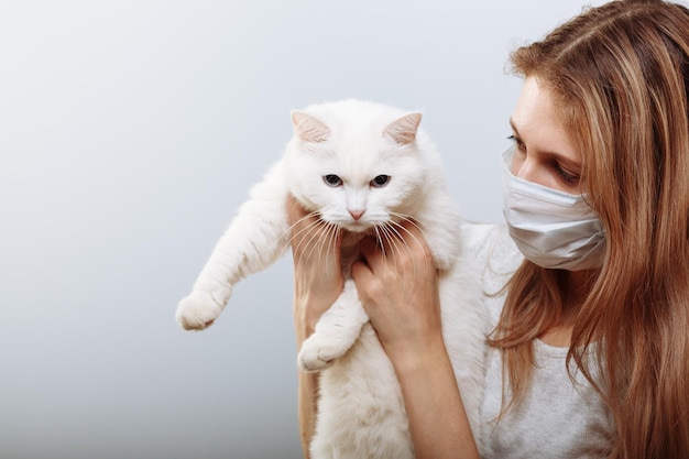 보호용 수술용 마스크를 쓴 여성이 얼굴 마스크에 고양이 애완동물을 안고 있다