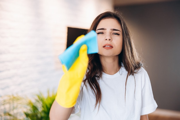 Donna in guanti gialli protettivi che puliscono e puliscono la polvere nella sua casa, primo piano. Foto Premium