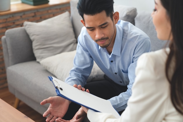 Woman psychiatrist talking with asian young man patient about his illness at hospital healthcare center