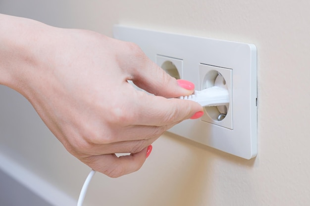 The woman pulls the electrical plug out of the socket wire. Safe use of electrical household appliances at home. Saving electrical energy.