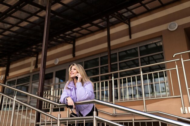 A woman in a purple jacket speaks on the phone on the stairs at the entrance to a residential