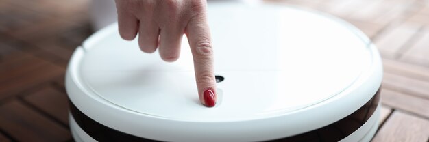 Woman pushing button in robot vacuum cleaner closeup. Repair of household appliances concept