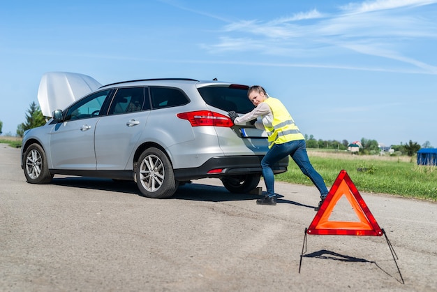 Woman pushing her broken car on roadside