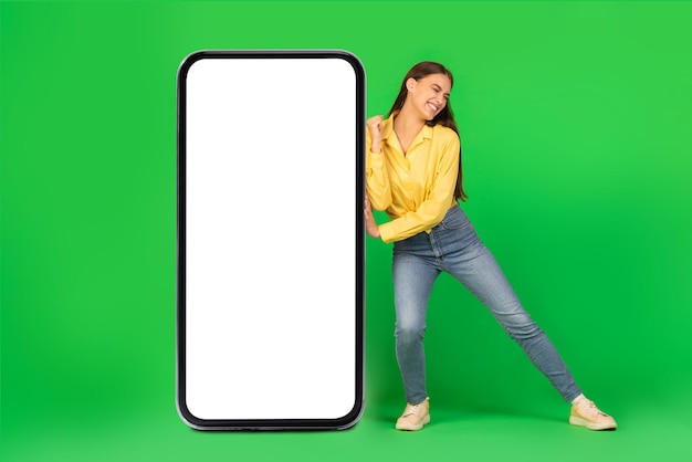 Woman pushing huge smartphone with empty screen on green background