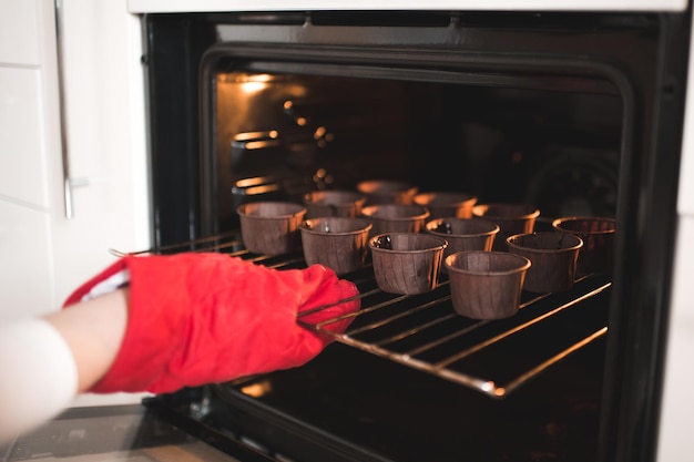 Woman put batter for chocolate cupcakes in oven