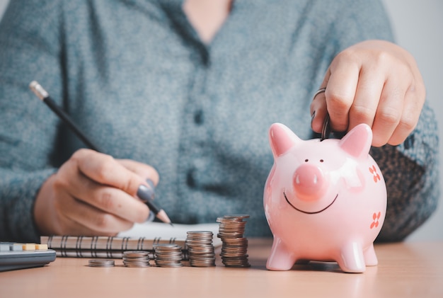 Woman put coin to pink piggy bank,