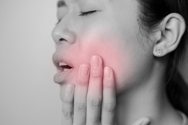 Photo woman put her hand on her cheek due to toothache. asian  woman is suffering of toothache. young woman with of toothache on a gray background.