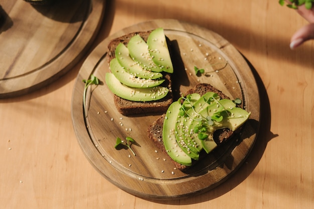 Woman put mustard seedlings on avocado sandwich with dark rye bread made with fresh sliced avocados