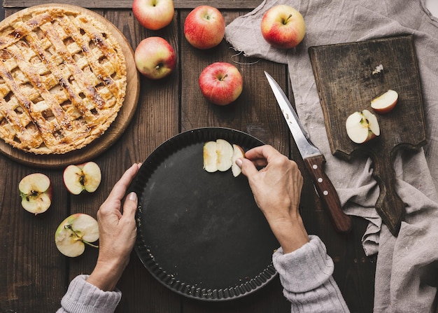 A woman puts apple slices in a round baking sheet on the table next to the ingredients