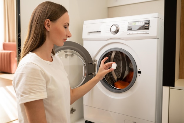 woman puts a capsule of washing powder in the washing machine on dirty laundry the woman turns on