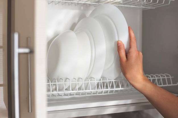 A woman puts a clean white plate on the kitchen shelf closeup