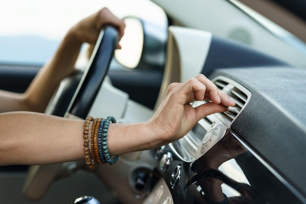 Woman puts hand on panel vent to check cold air flow sitting at
driver seat in car on hot summer day