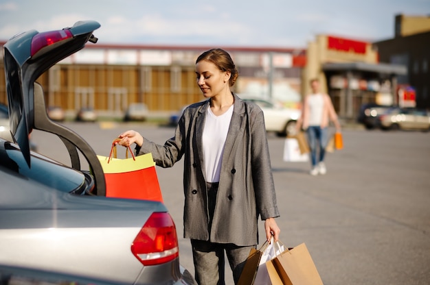 Woman puts her purchases in the trunk on parking