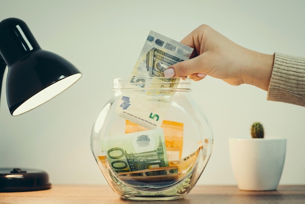 Woman putting 5 euro banknote to the glass bank Saving money for a dream toned image