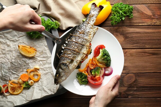 Photo woman putting baked fish on plate with vegetables