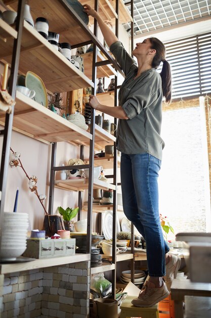 Photo woman putting ceramics on shelf