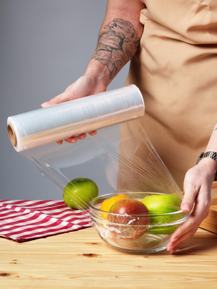 Photo woman putting cling filmover bowl of fresh fruit at wooden table