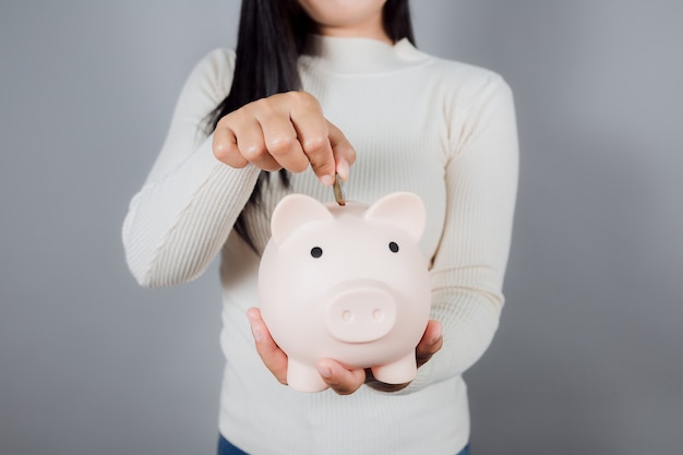 Woman Putting Coin In Piggy Bank on gray background