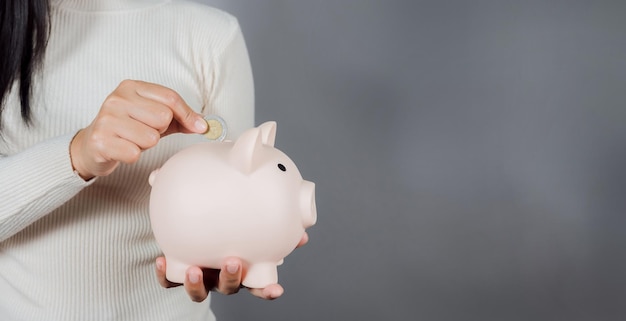 Woman Putting Coin In Piggy Bank on gray background