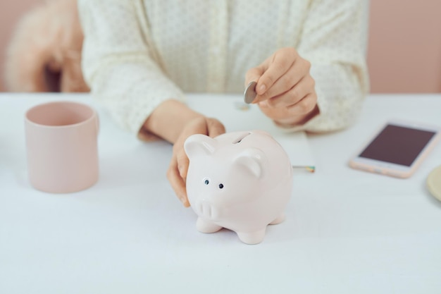 Woman Putting Coin In Piggy Bank Indoors