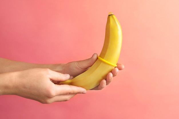 Woman putting condom on banana on color background